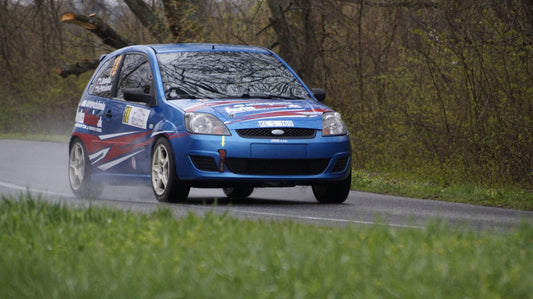 a small blue car driving down a country road